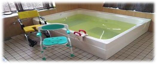大きな浴槽の手前に、黄色い入浴用の車いすと、緑色のシャワーチェアが置いてある