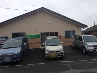平屋の建物。入口の横に緑色の「みやびデイサービス」の看板があり、前の駐車場に車が3台とまっている